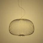 The low, wide drum-shaped wire-cage Clérachic pendant in a gold finish, on a warm yellow backdrop.