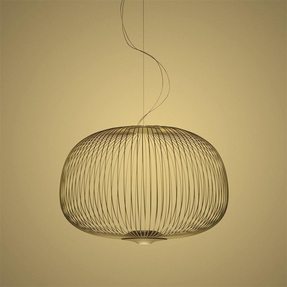 The low, wide drum-shaped wire-cage Clérachic pendant in a gold finish, on a warm yellow backdrop.