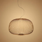 The low, wide drum-shaped wire-cage Clérachic pendant in a copper finish, glowing on an amber backdrop.