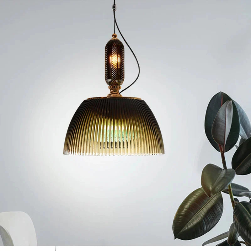 The Clérachic ribbed smoked-glass pendant hangs above a reading nook, its faceted amber finial glowing beside a leafy rubber plant.