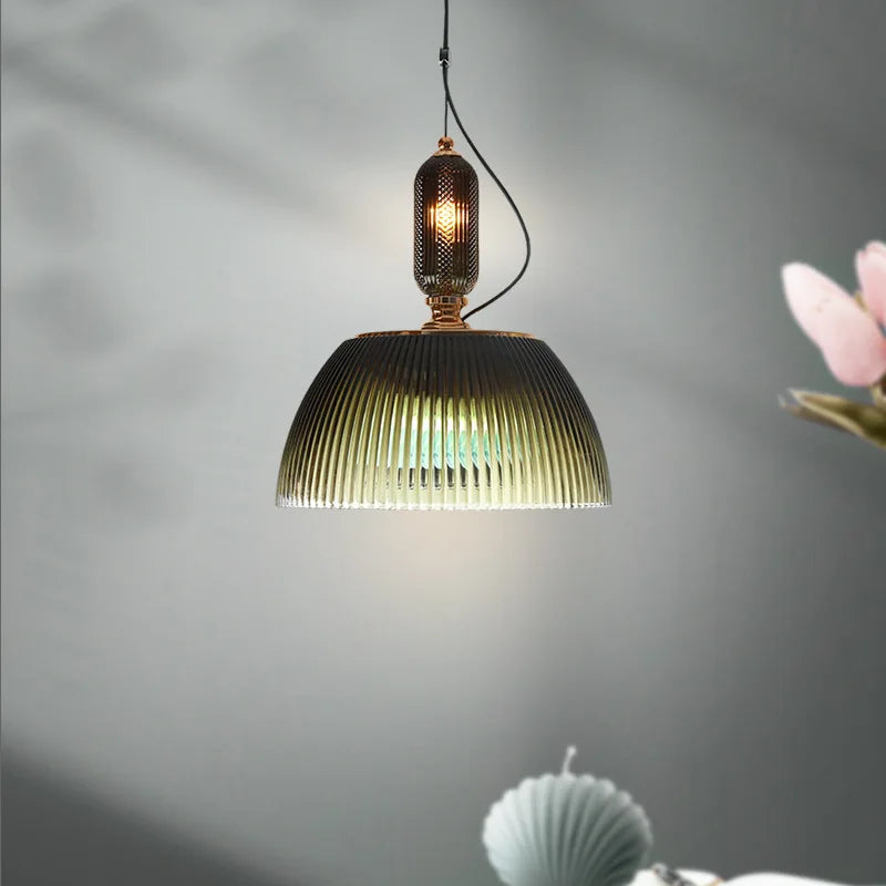 The Clérachic ribbed pendant glows amber against a soft gray backdrop, styled here with a spray of pink blossom.