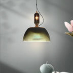 The Clérachic ribbed pendant glows amber against a soft gray backdrop, styled here with a spray of pink blossom.