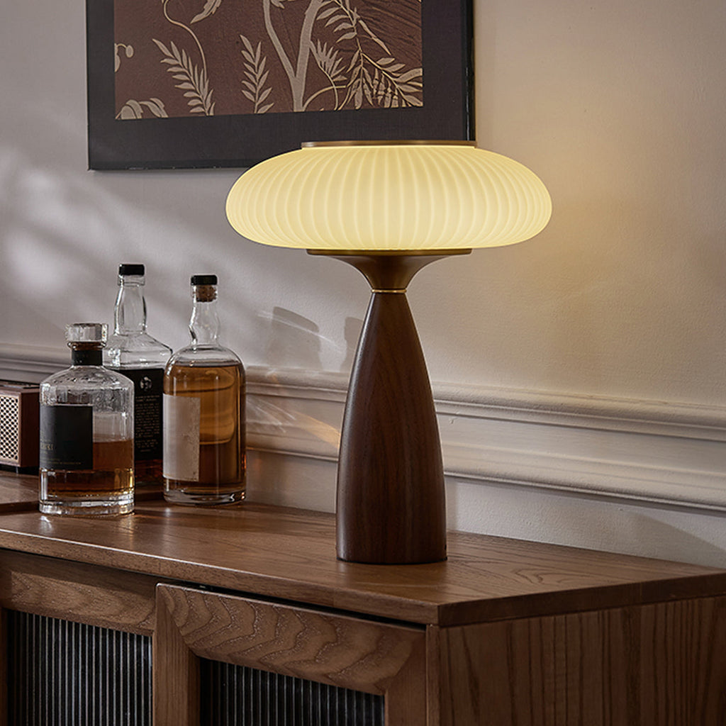 A Clérachic ribbed table lamp glowing on a walnut sideboard beside three whisky bottles, under a botanical print.