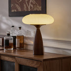 A Clérachic ribbed table lamp glowing on a walnut sideboard beside three whisky bottles, under a botanical print.
