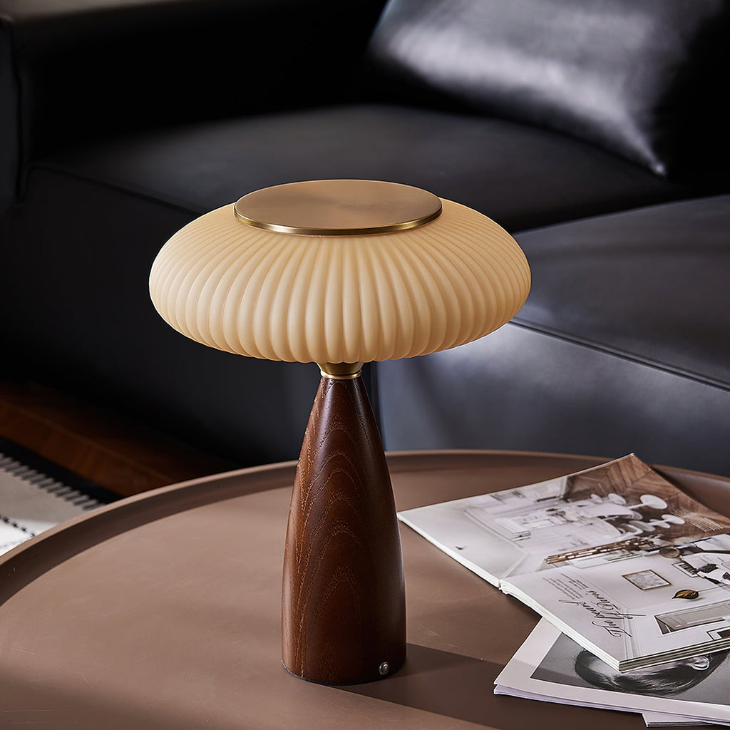 Close framing of this Clérachic lamp on a round brown coffee table, a black leather sofa behind and open magazines beside it.