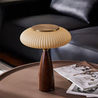 Close framing of this Clérachic lamp on a round brown coffee table, a black leather sofa behind and open magazines beside it.