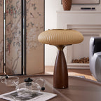 This Clérachic table lamp on a low round table with a glass teapot and magazine, in front of a painted folding screen.