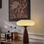 Lit ribbed shade of this Clérachic lamp on a wooden sideboard under a botanical print, with whisky bottles at its left.
