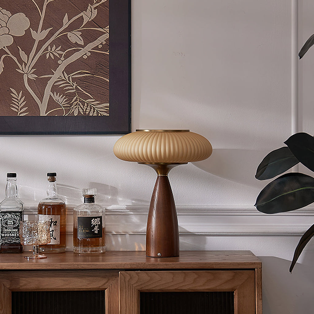 Unlit Clérachic ribbed lamp on a walnut sideboard in front of a botanical print, with whisky bottles and a plant beside it.