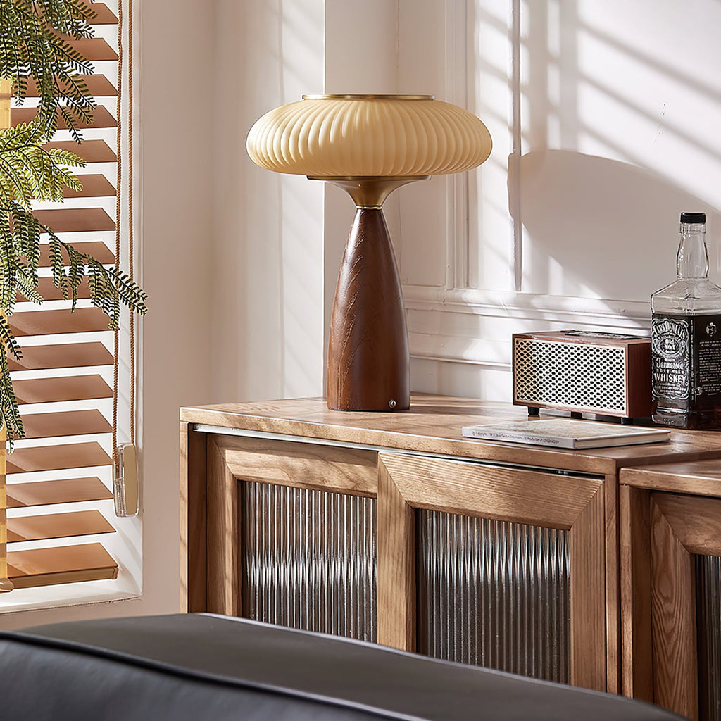 This Clérachic lamp on a slatted-glass wooden sideboard beside a retro speaker and a bottle, with sunlit blinds at the window.
