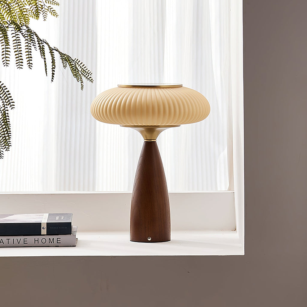 Clérachic table lamp on a white window ledge with stacked books, the sheer curtains and a fern frond behind it.