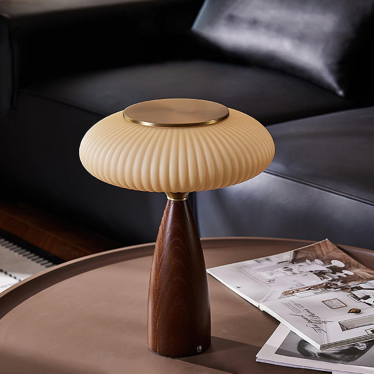 Brass-topped shade of this Clérachic table lamp on a round table, with a leather sofa behind and magazines on the surface.