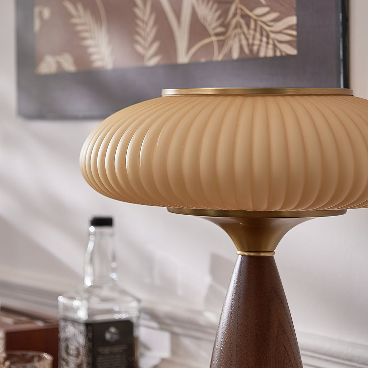 Close view of the ribbed cinnamon shade and brass collar of this Clérachic lamp, with a bottle and a botanical print behind.
