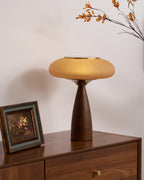 This Clérachic table lamp on a walnut chest of drawers beside a framed floral picture, with autumn leaves above.