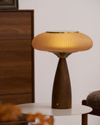 Closer view of this Clérachic table lamp lit on a round white table, a dark chest of drawers and a cushioned chair behind.