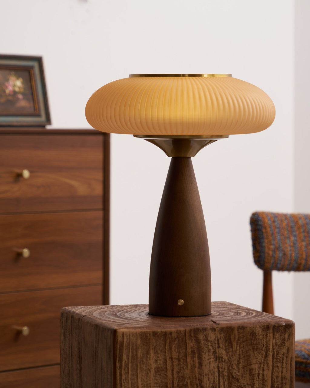 Clérachic table lamp on a wooden block next to a framed picture, its shade and brass collar over a walnut-colour base.