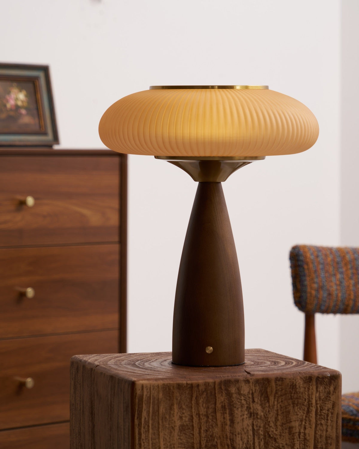 Clérachic table lamp on a wooden block next to a framed picture, its shade and brass collar over a walnut-colour base.