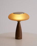 This Clérachic table lamp, lit, on a round white table against a pale grey wall, its cinnamon shade glowing warmly.