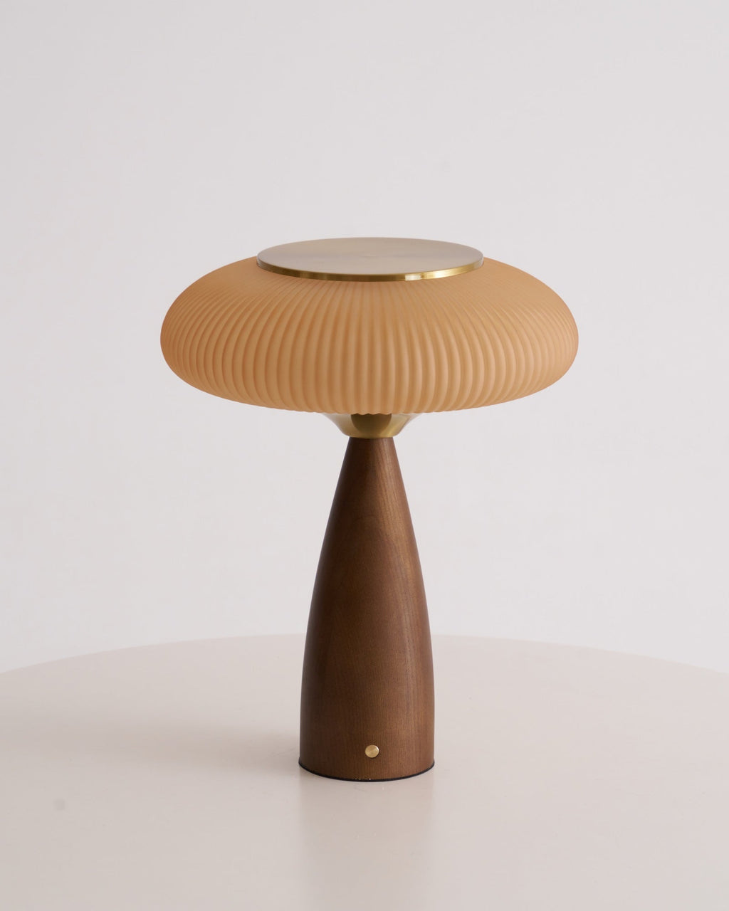 Unlit Clérachic table lamp on a white table against grey, showing the cinnamon shade, brass top and tapered walnut base.