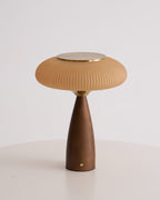 Unlit Clérachic table lamp on a white table against grey, showing the cinnamon shade, brass top and tapered walnut base.