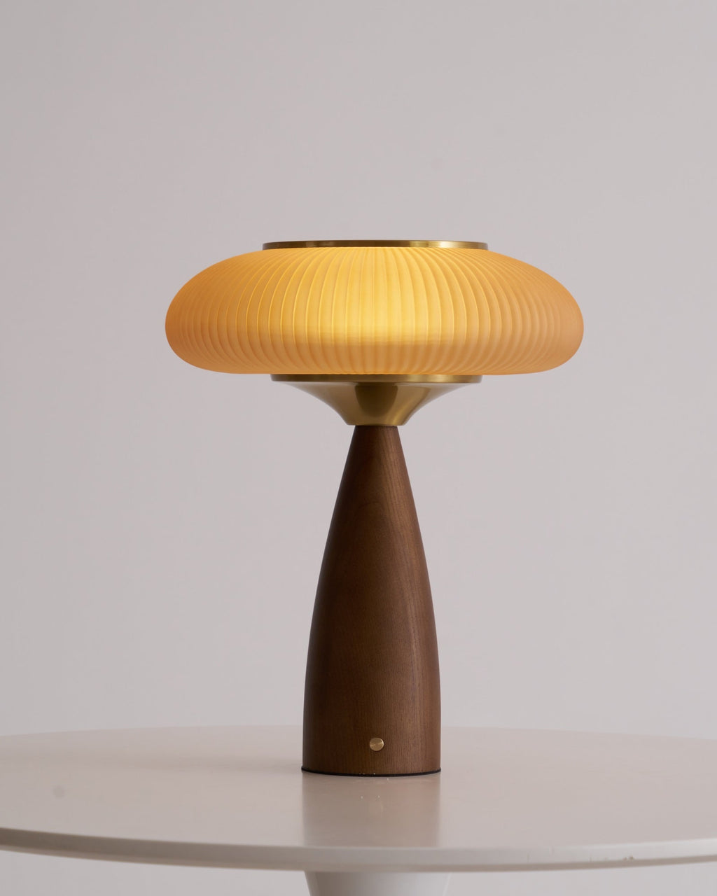 Lit Clérachic table lamp seen from a lower angle on a white table, the brass collar bright under the glowing shade.