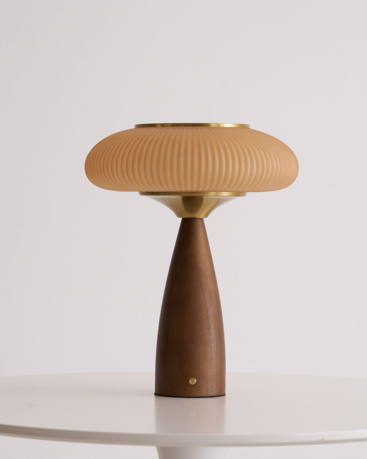 Clérachic table lamp on a white table, unlit, the ribbed cinnamon shade above a brass collar and a small brass button.