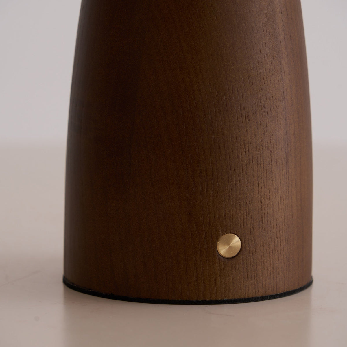 Close view of the walnut-colour base of this Clérachic lamp, with the small brass touch button near the foot.