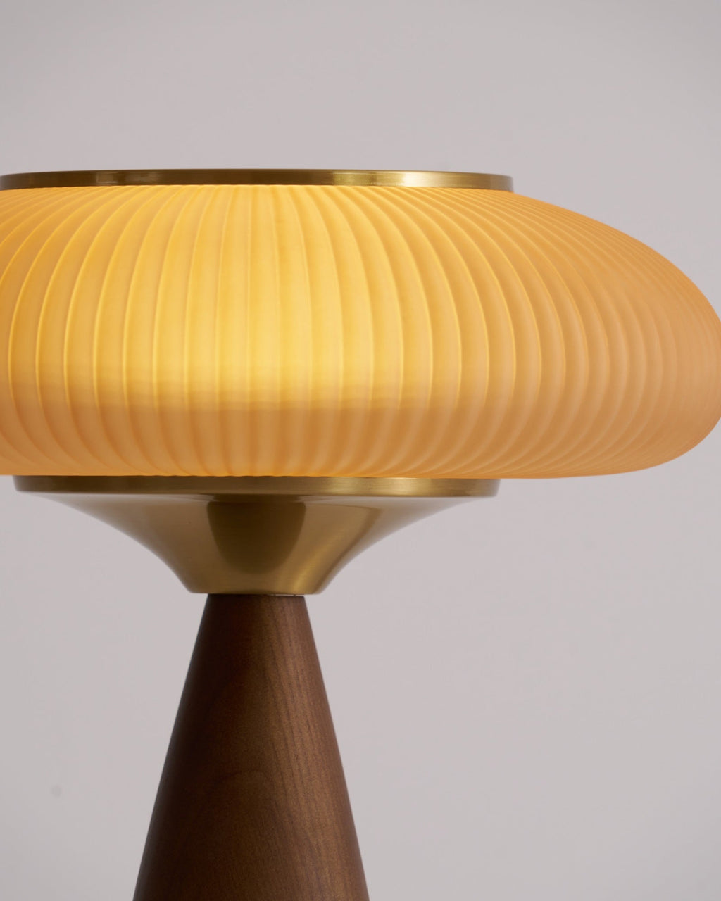 Close view of the lit ribbed shade, brass collar and top of the walnut base on this Clérachic table lamp.