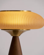 Close view of the lit ribbed shade, brass collar and top of the walnut base on this Clérachic table lamp.
