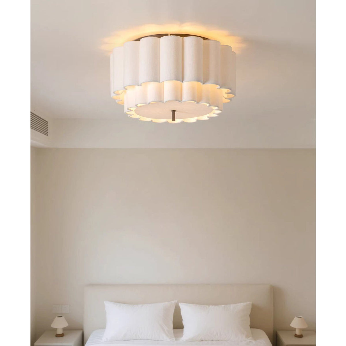 Above a bed with white pillows and small bedside lamps, this Clérachic ceiling light glows from a pale ceiling.