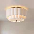 Close view of this Clérachic ceiling light on the ceiling, its scalloped white fabric tiers lit warm around the edge.