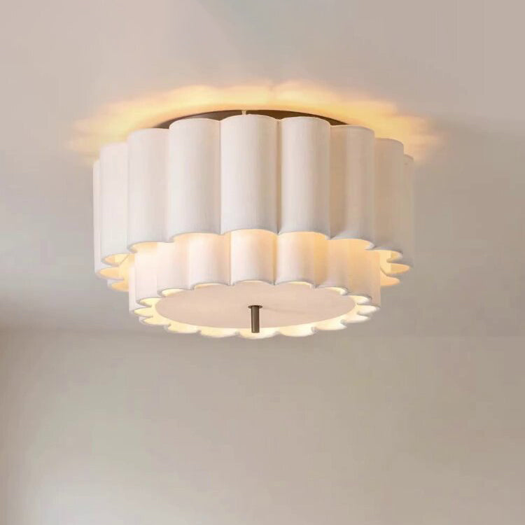 Close view of this Clérachic ceiling light on the ceiling, its scalloped white fabric tiers lit warm around the edge.