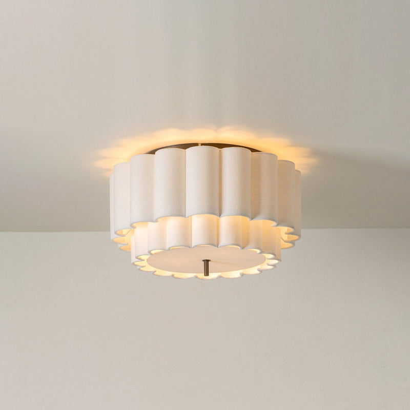 A Clérachic ceiling light seen against a plain cream wall, its ribbed shade lit with a soft glow on the ceiling around it.
