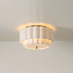 A Clérachic ceiling light seen against a plain cream wall, its ribbed shade lit with a soft glow on the ceiling around it.
