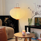 Clérachic oval rice-paper floor lamp lit beside a black lacquered cabinet painted with a koi, a candle burning on the round wooden table in front of it.