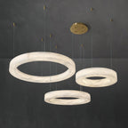 Clérachic three-ring chandelier lit in a grey interior, the tiered alabaster hoops staggered on brass cables.