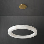The Clérachic chandelier shot at an angle, alabaster hoop and brass canopy read against dark concrete.