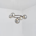 A Clérachic ring-frame pendant with 5 smoked mirrored glass globes hangs from thin cables in a bright corner room.