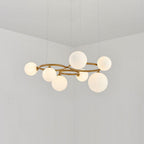 The brass Clérachic ring-frame pendant carries 7 glowing opal glass globes, photographed in a bright room.