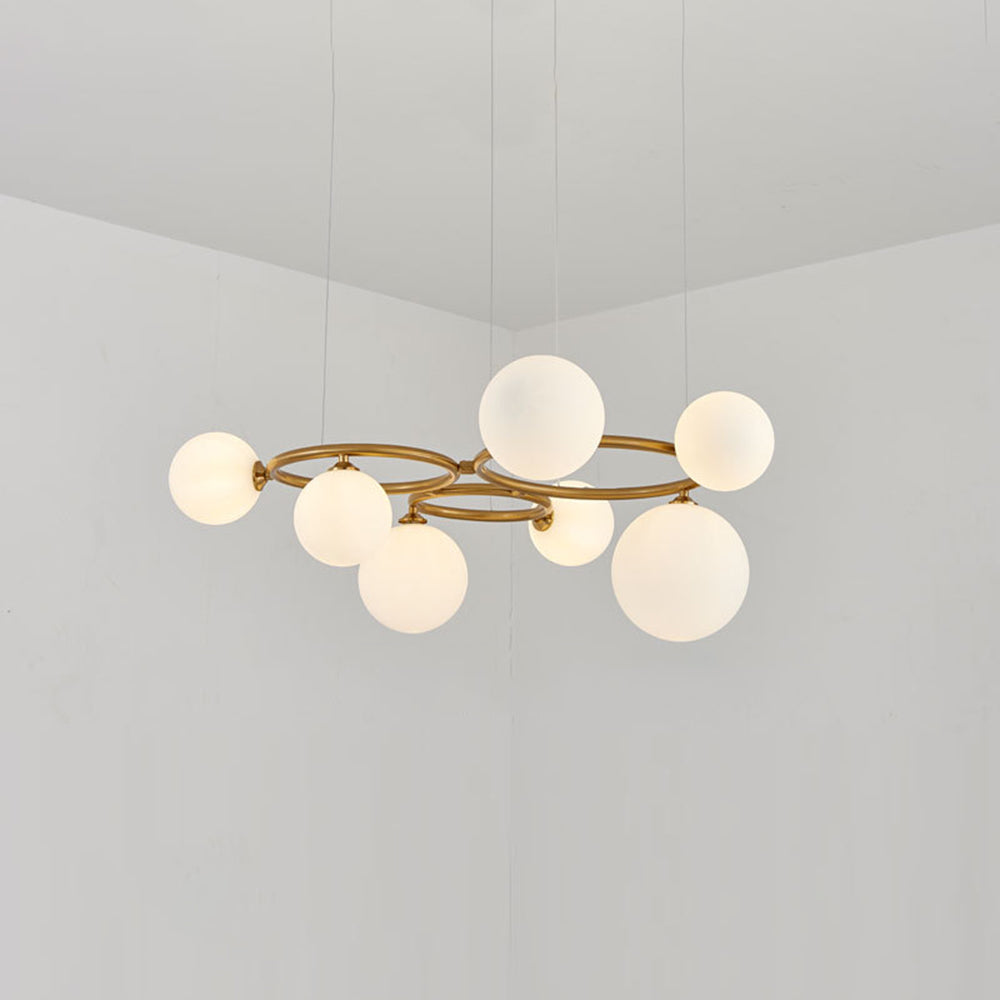 The brass Clérachic ring-frame pendant carries 7 glowing opal glass globes, photographed in a bright room.