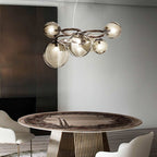 A Clérachic ring-frame pendant with amber-glowing smoked glass globes hangs above an oval stone dining table.