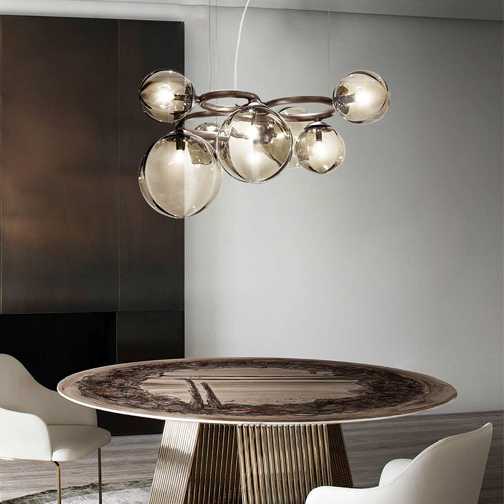A Clérachic ring-frame pendant with amber-glowing smoked glass globes hangs above an oval stone dining table.