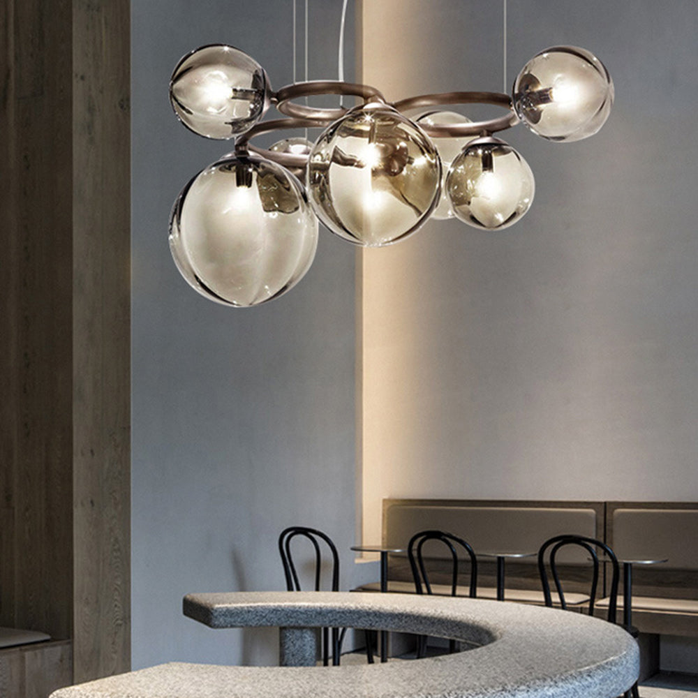 A Clérachic ring-frame pendant with amber-glowing smoked glass globes hangs above a curved stone café bench.
