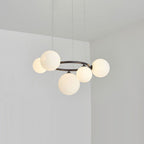 Five glowing opal glass globes ring the black frame of this Clérachic pendant in a plain corner room.