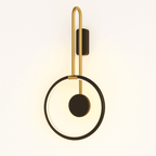 Clérachic wall light with a black ring, black disc and brass-toned arm, glowing warm against a soft cream backdrop.