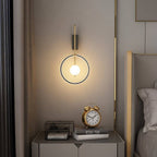 Clérachic ring wall light with a brass-toned arm and a glowing white glass ball above a bedside table with a gold clock.