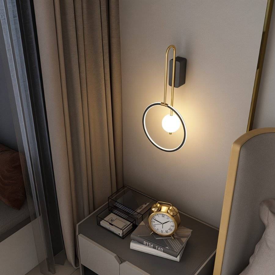 Clérachic black ring wall light with a lit glass ball, seen from above a bedside table with a gold clock and books.