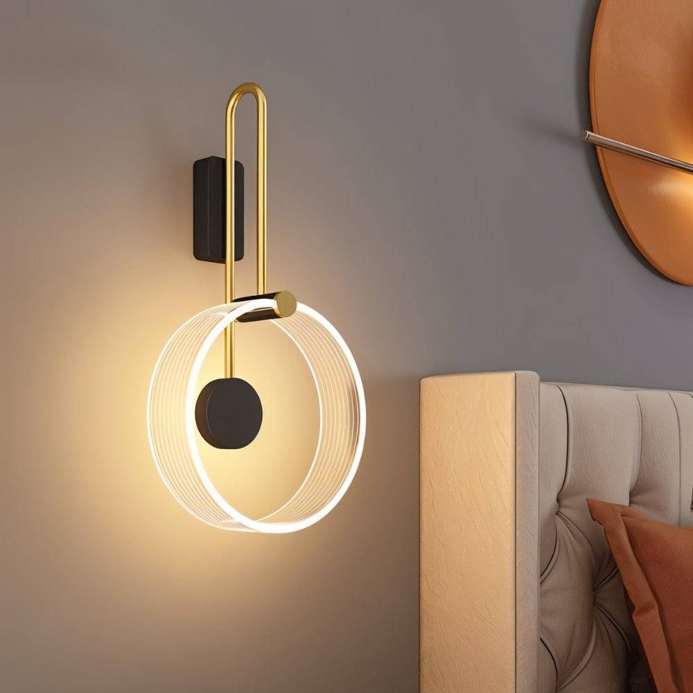 Clérachic wall light with a clear fluted acrylic ring, black disc and brass-toned arm, glowing warm above a bed.