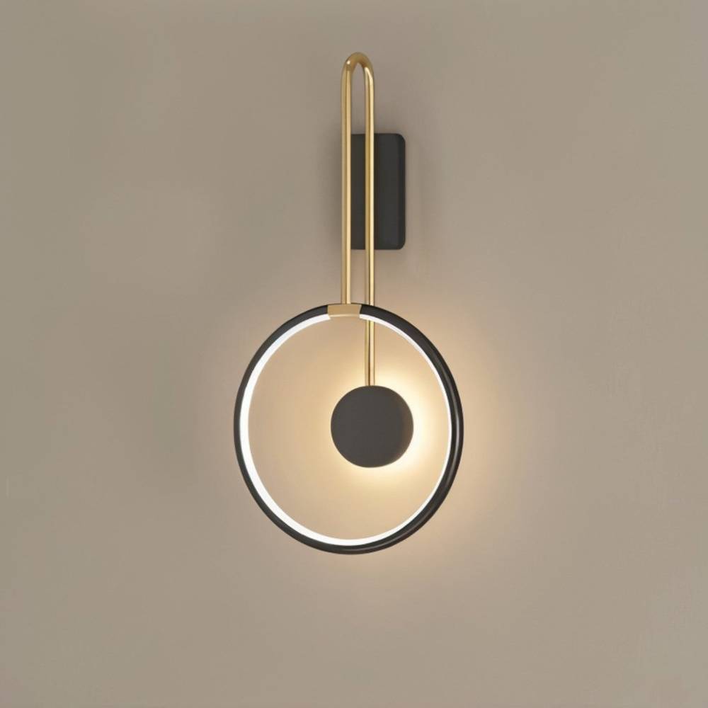 Clérachic black ring wall light with a brass-toned U-shaped arm and a black disc, glowing warm on a taupe wall.