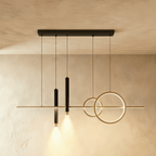 Clérachic gold and black pendant light with a linear bar, two rings and two spotlight cylinders glowing on a limewash wall.